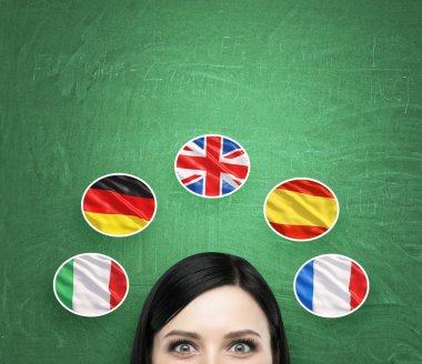 A concept of foreign language studying process. A foreseen of the brunette girl surrounded by icons of european flags. Green chalkboard background.