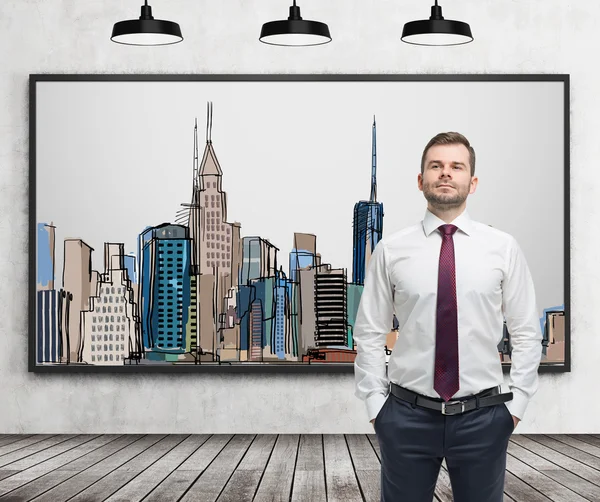 A handsome man in formal clothes stands in front of the picture of New York City on the wall. Wooden floor, concrete wall and three black ceiling lights. — Stock Photo, Image