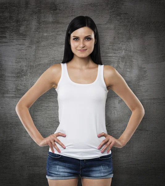 Uma mulher morena em um top de tanque branco e denims. As mãos estão nos bolsos. Tábua de giz preto no fundo . — Fotografia de Stock