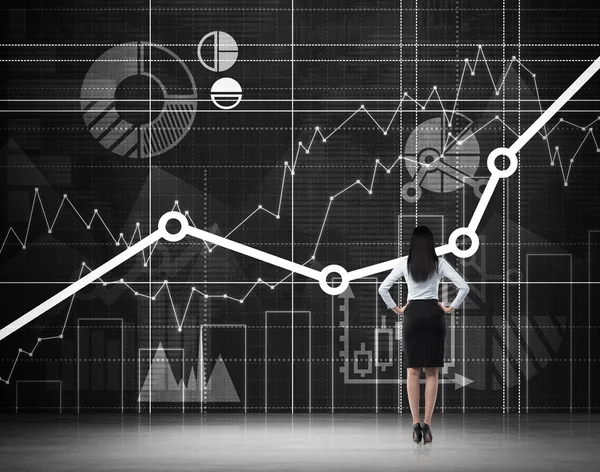 Rear view of the full length brunette in formal clothes who is looking at the drawn financial charts on the black wall. — Stock Photo, Image