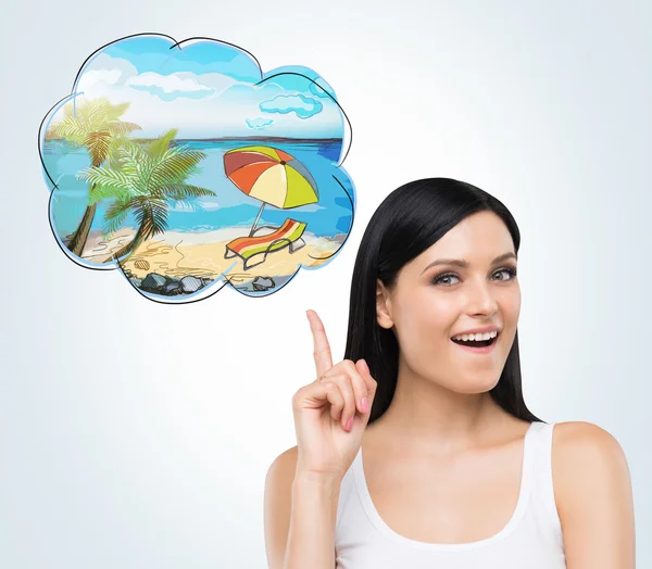 A portrait of a brunette woman who dreams about summer vacation on the beach. A nice summer place is drawn in the thought bubble. Concrete wall. — Stock Photo, Image