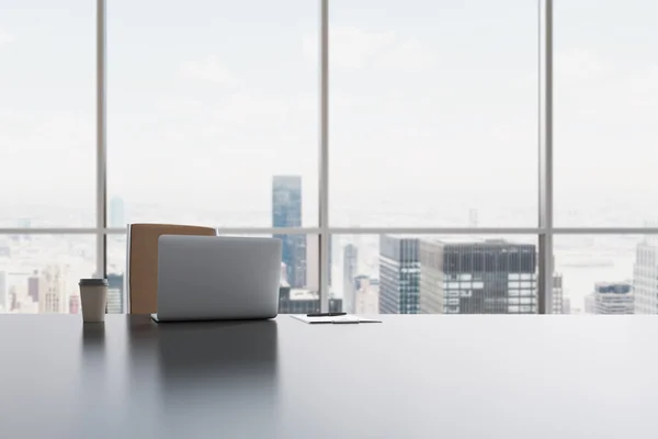 A workplace in a modern panoramic office in Manhattan, New York City. A laptop, notepad and a coffee cup are on the white table. 3D rendering. — Stok fotoğraf