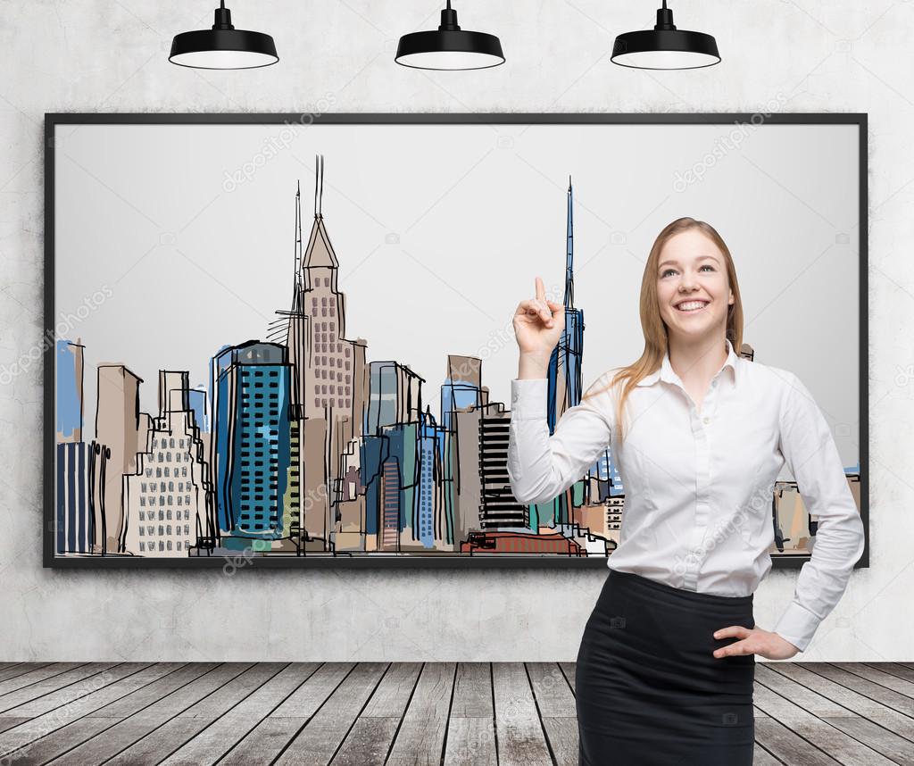 A beautiful lady is pointing out the picture of New York City on the wall. Wooden floor, concrete wall and three black ceiling lights.