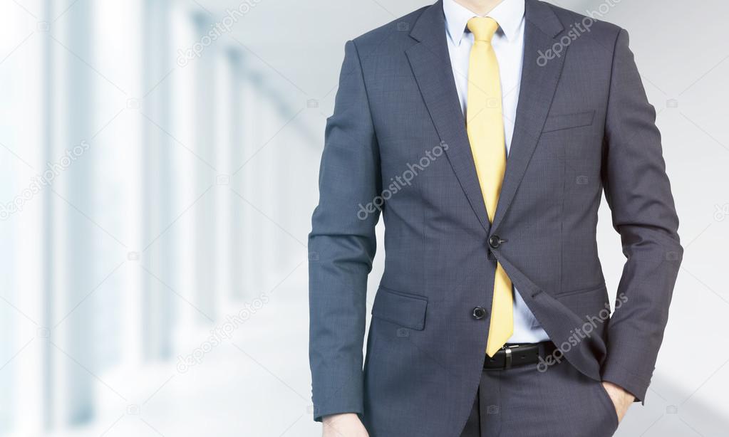 Close-up of a professional in formal suit with the hand in the pocket. Bright modern office in blur on the background.