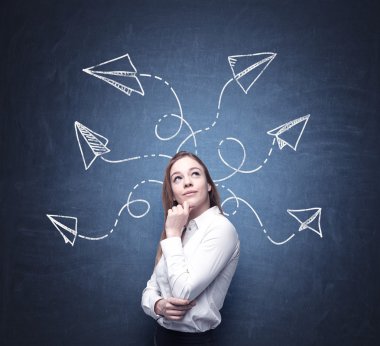 A beautiful woman is pondering about possible solutions of the complicated problem. Many arrows with different directions are drawn around her head. Blue chalkboard as a background.