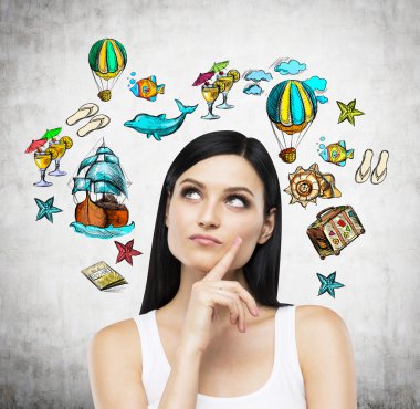 A portrait of thoughtful brunette who is surrounded by summer vacation icons which are drawn on the concrete wall.
