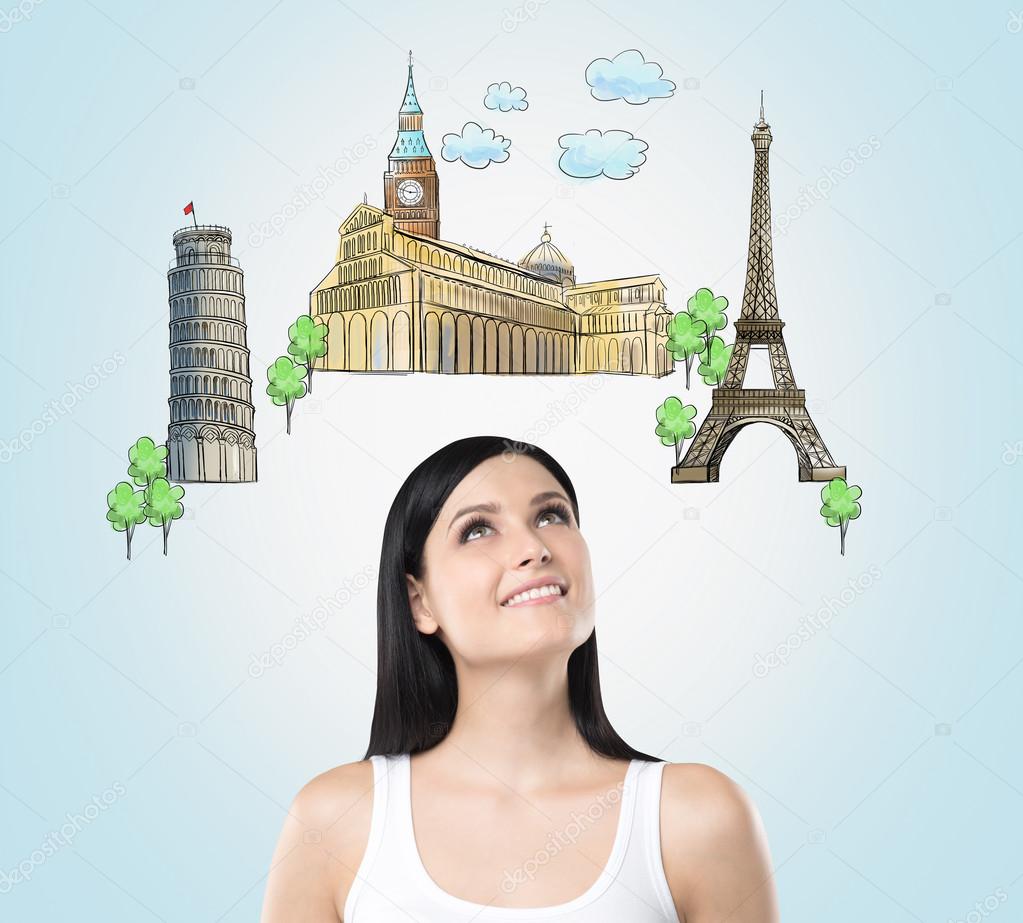 A beautiful brunette is looking up by dreaming about the visiting of the most famous european cities. The concept of tourism and sightseeing. Light blue background.