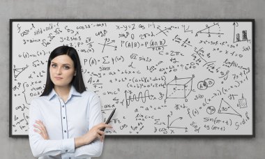 A beautiful brunette is pondering about the solution of complicated analytical problem. Math formulas are written down on the whiteboard. Concrete wall. clipart