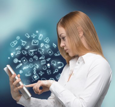 A side view of beautiful young woman who browses some information in the Innternet using the tablet. Social media hologram icons are flying in the air.