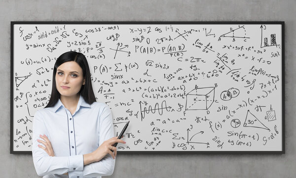 A beautiful brunette is pondering about the solution of complicated analytical problem. Math formulas are written down on the whiteboard. Concrete wall.