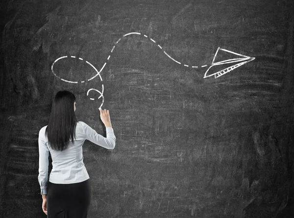 Rear view of brunette in formal clothes who is drawing an arrow as a concept of possible solution of the complicated problem. Black chalkboard on the background. — 스톡 사진