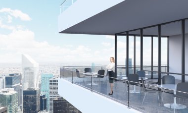 A woman is looking at New York standing on the terrace in a modern skyscraper with panoramic windows.