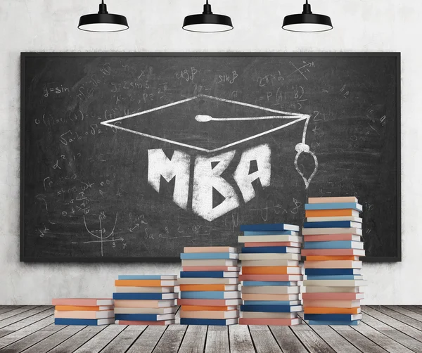 Una escalera está hecha de libros coloridos. Un sombrero de graduación se dibuja en la pizarra negra. Concepto de MBA. Pared de hormigón, suelo de madera y tres luces de techo negras . —  Fotos de Stock