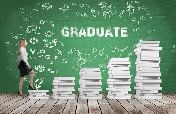 A woman is going up using a stairs which are made of white books. The word graduate is on the green chalkboard. Wooden floor. — Stock Photo, Image