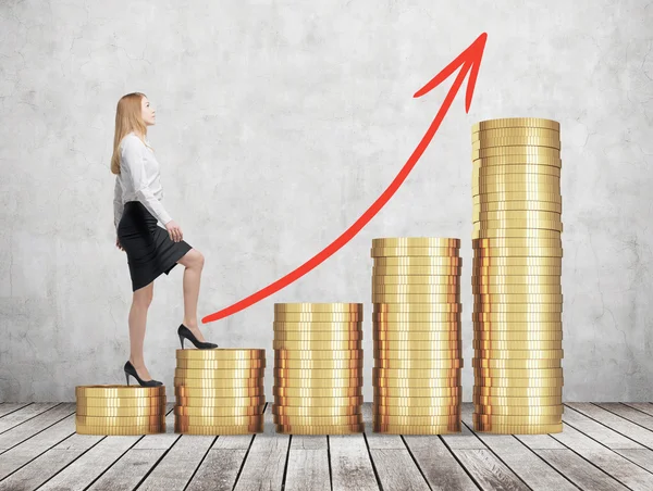 A woman in formal clothes is going up using a stairs which are made of golden coins. Red arrow is drawn on the wall. A concept of success. Concrete wall and wooden floor. — Stock Photo, Image