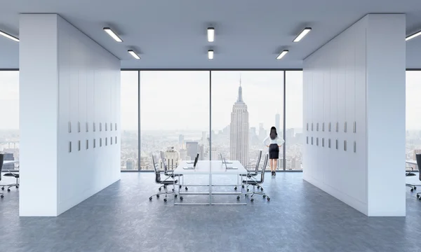 Vue arrière d'une brune qui regarde par la fenêtre dans un bureau panoramique moderne. Vue sur New York . — Photo