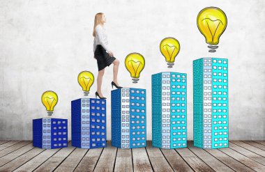 A woman in formal clothes is going up using a stairs which are made of houses with lightbulbs. A concept of new ideas and success. Concrete background.