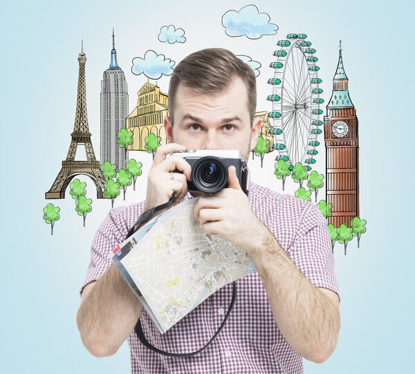 A front view of the handsome tourist with camera. Drawn sketches of the most famous touristic places on the light blue background. The concept of tourism and sightseeing.