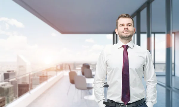 A handsome confident businessman stands on the terrace in the skyscraper with panoramic windows. New York view. Sunset. — Stock Fotó