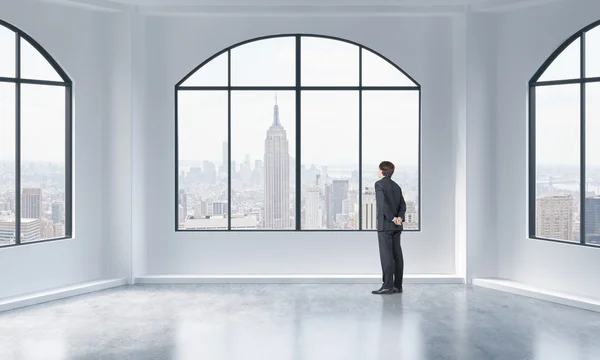 Rear view of a person in formal suit who is looking out the window in a modern loft interior. New York city view. — Stockfoto