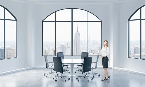 A beautiful young professional stands in modern conference room with New York city view. — Stock fotografie