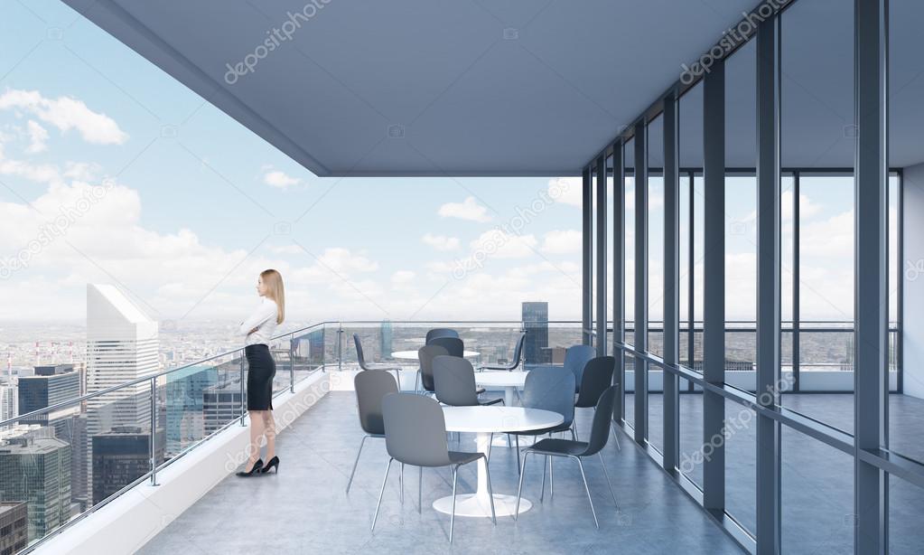 A woman is looking at New York standing on the terrace in a modern skyscraper with panoramic windows.