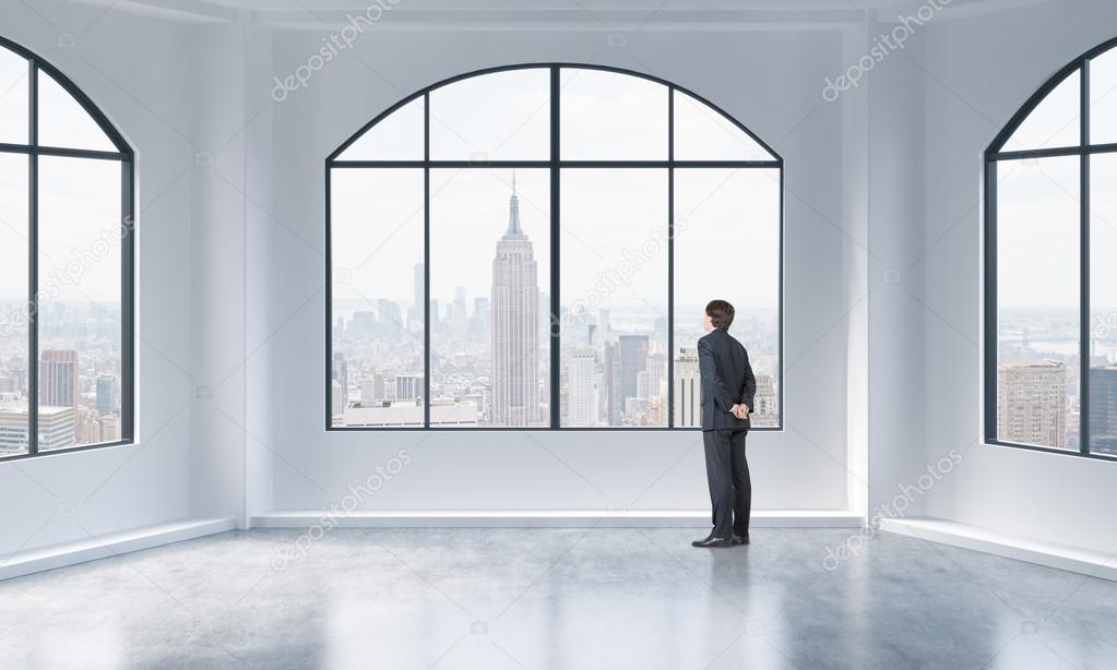 Rear view of a person in formal suit who is looking out the window in a modern loft interior. New York city view.