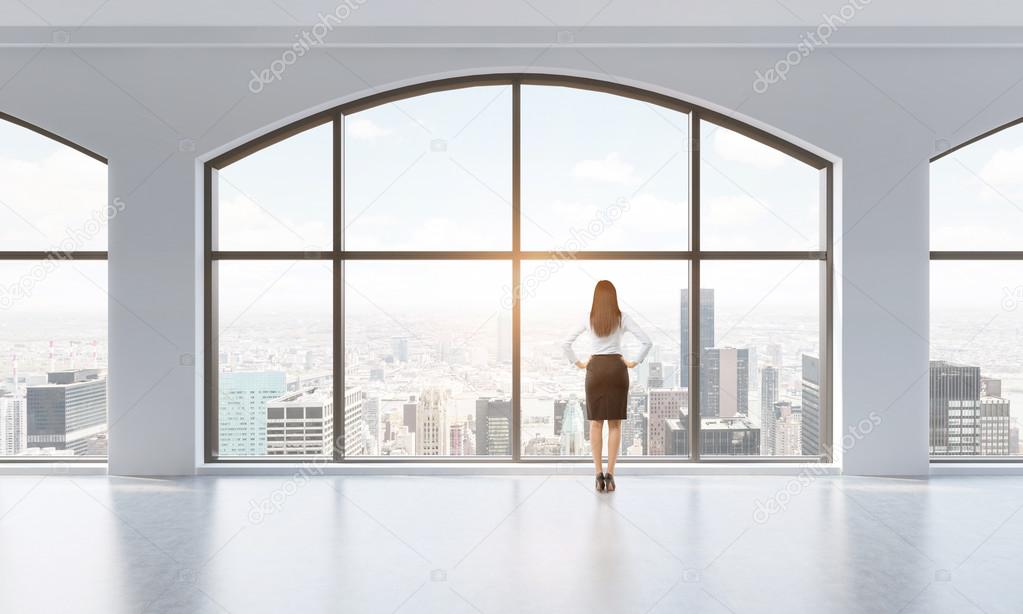 Rear view of a woman in formal clothes who is looking out the window in a modern clean interior with huge panoramic windows. New York city view. Toned Image.