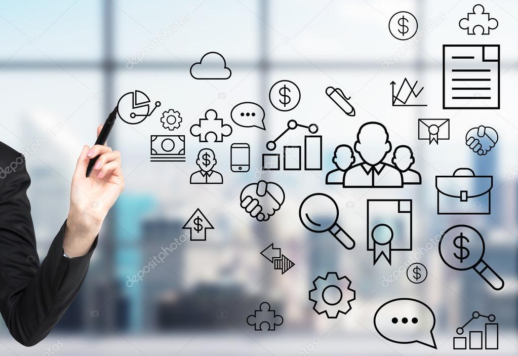 A woman's hand is drawing some business icons on the glass screen. Modern panoramic office with New York view in blur on the background.