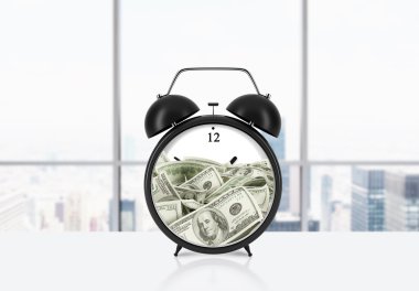 An alarm clock with dollar bills inside is on the table. The concept of 'time is money' and a time management. Panoramic New York office background.