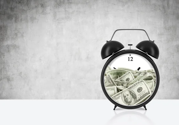 An alarm clock with dollar bills inside is on the table. The concept of 'time is money' and a time management. Concrete background. — Stockfoto