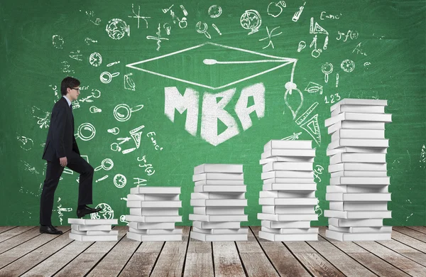 Мужчина поднимается по лестнице, которая сделана из белых книг, чтобы добраться до выпускной шляпы. Письменное слово MBA нарисовано на зеленой доске, которая символизирует профессиональное бизнес-образование . — стоковое фото