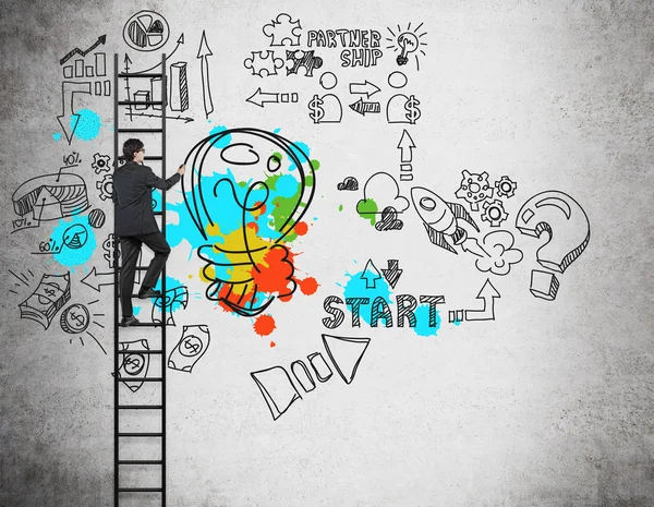 Um empresário na escada está desenhando ícones de gestão de negócios e uma lâmpada colorida na parede de concreto. O conceito do brainstorm ou um start up . — Fotografia de Stock