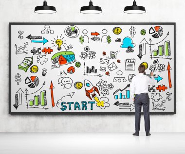 Resmi kıyafetler bir işadamı bir renkli çizim iş çizelgeleri ve beyaz tahta üzerinde simgeler. Yeni bir iş kurmak bir kavram. Orada beton duvar ve üç siyah tavan ışığı.