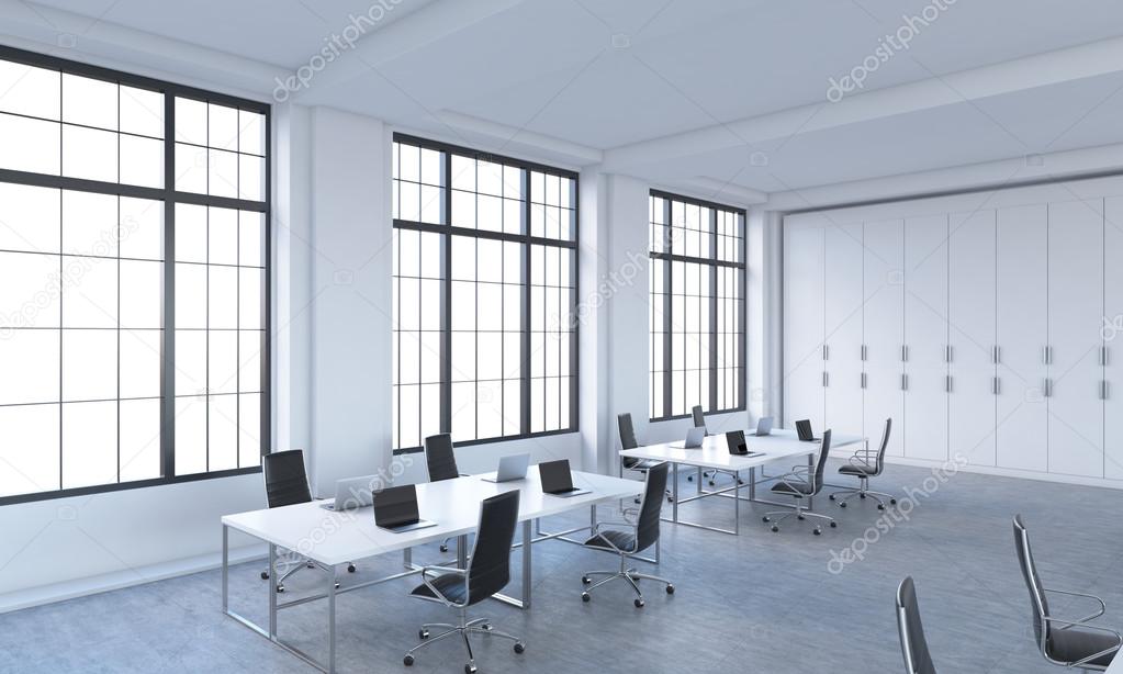 Workplaces in a bright modern open space loft office. White tables equipped with modern laptops and black chairs. White copy space in the panoramic windows. 3D rendering.