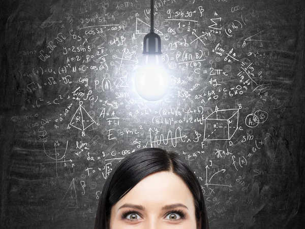 A forehead of brunette woman who is thinking about solution of complicated math problem. Math formulas are on the black chalkboard. A light bulb as a concept of a solution. Analytics approach. — Stockfoto