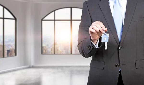 Un hombre con traje formal tiene una llave en un apartamento o oficina panorámica loft moderno. Alquile o compre una casa u oficina nueva. Vista de Nueva York. Una puesta de sol . — Foto de Stock