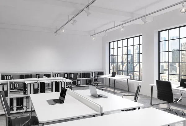 Workplaces in a bright modern loft open space office. Tables equipped with laptops; corporate documents' shelves. New York in the panoramic windows. 3D rendering.