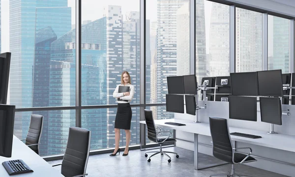 A young lady in formal clothes holds a black document folder in the modern panoramic office in Singapore. White tables equipped with modern trader\'s stations and black chairs.