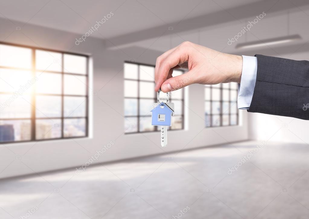 A man in formal suit holds a key in a modern loft panoramic apartment or office. Rent or buy new home or office. New York view. A sunset.