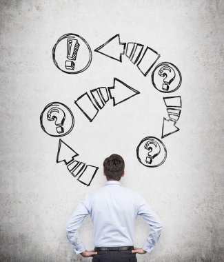 Rear view of a businessman who is looking at the concrete wall with drawn arrows with exclamation and question marks.