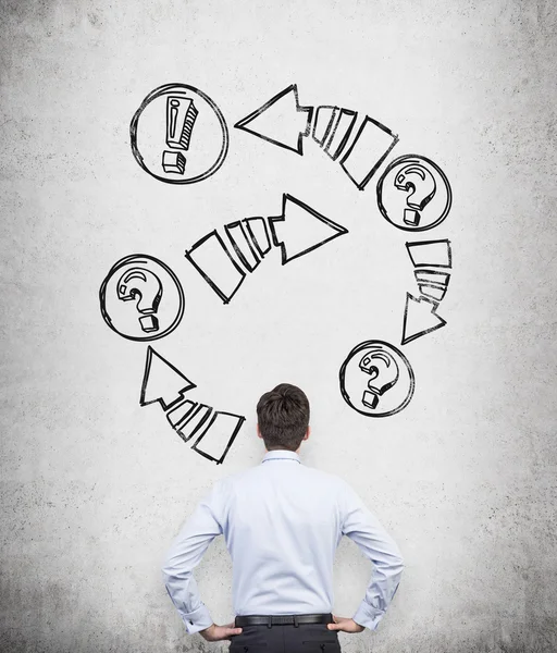 Rear view of a businessman who is looking at the concrete wall with drawn arrows with exclamation and question marks. — Stock Photo, Image