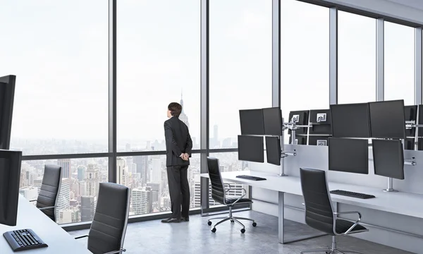 Rear view of a man in formal suit who is looking out the window in the modern panoramic office with New York view. White tables equipped with modern trader's stations and black chairs. — Φωτογραφία Αρχείου