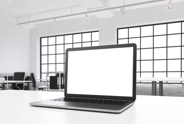A workplace in a bright modern loft open space office. A working desk is equipped with a modern laptop with white copy space in the screen. Docs shelves. White copy space in the windows. 3D rendering.