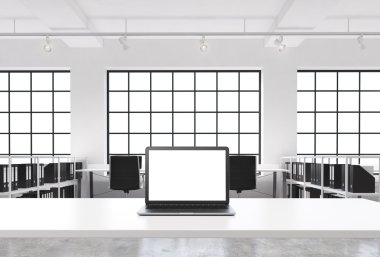 A workplace in a bright modern loft open space office. A working desk is equipped with a modern laptop with white copy space in the screen. Docs shelves. White copy space in the windows. 3D rendering.