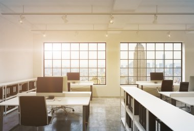 Workplaces in a sunset loft open space office. Tables are equipped with computers; book shelves. New York panoramic view. A concept of a high quality consulting services. Toned image. 3D rendering.