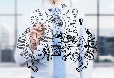 A businessman is drawing a business plan development sketch on the glass screen. A modern panoramic office in blur on the background. A light bulb as a concept of brainstorm. clipart