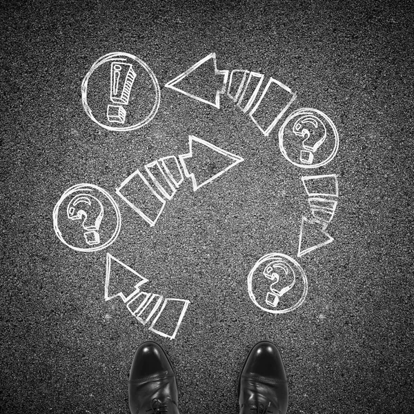 Top view of the formal man 's black shoes and drawn arrows with exclamation and question marks on asphalt . — стоковое фото