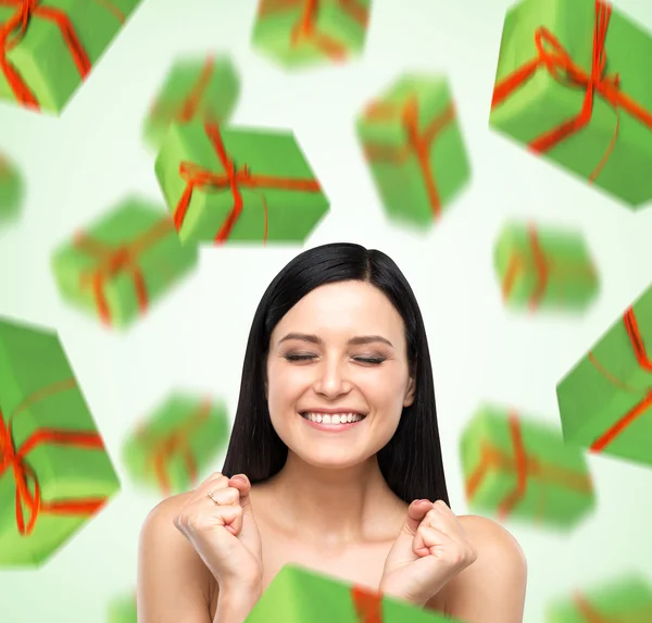 A portrait of dreaming woman with closed eyes who is imagining green gift boxes. Light green background. — Stock Photo, Image