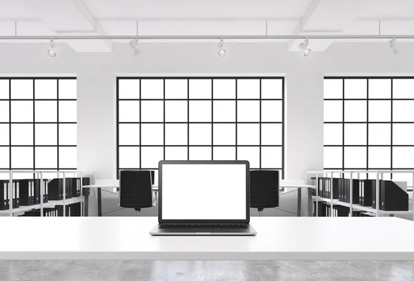 A workplace in a bright modern loft open space office. A working desk is equipped with a modern laptop with white copy space in the screen. Docs shelves. White copy space in the windows. 3D rendering. — Stockfoto